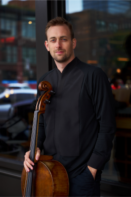 Man wearing a black button up shirt stands with a cello